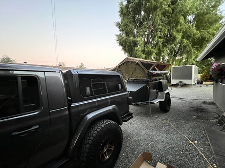 Dark truck with an overland trailer and rooftop tent deployed, a complete setup for an rv rental adventure.