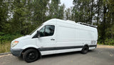 This white Mercedes Sprinter 3500 van, ideal for RV rental, is perfect for a road trip adventure. Parked by trees.