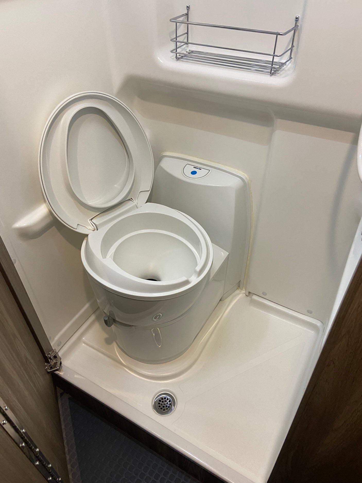 Compact RV rental wet bath featuring a modern Thetford toilet, integrated shower, and storage shelf.