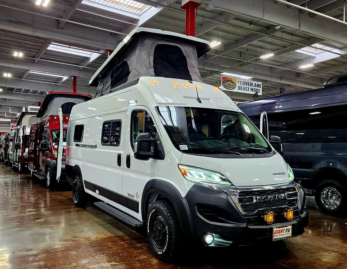 White Storyteller Overland camper vans in a showroom. Perfect #rvrental for overland adventures!|RV rental parked on a dirt road in a vibrant vineyard at sunset