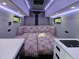 Cozy RV rental interior features a vibrant patterned bed, sleek induction cooktop, and bright LED strip lighting. Ideal for road trips.