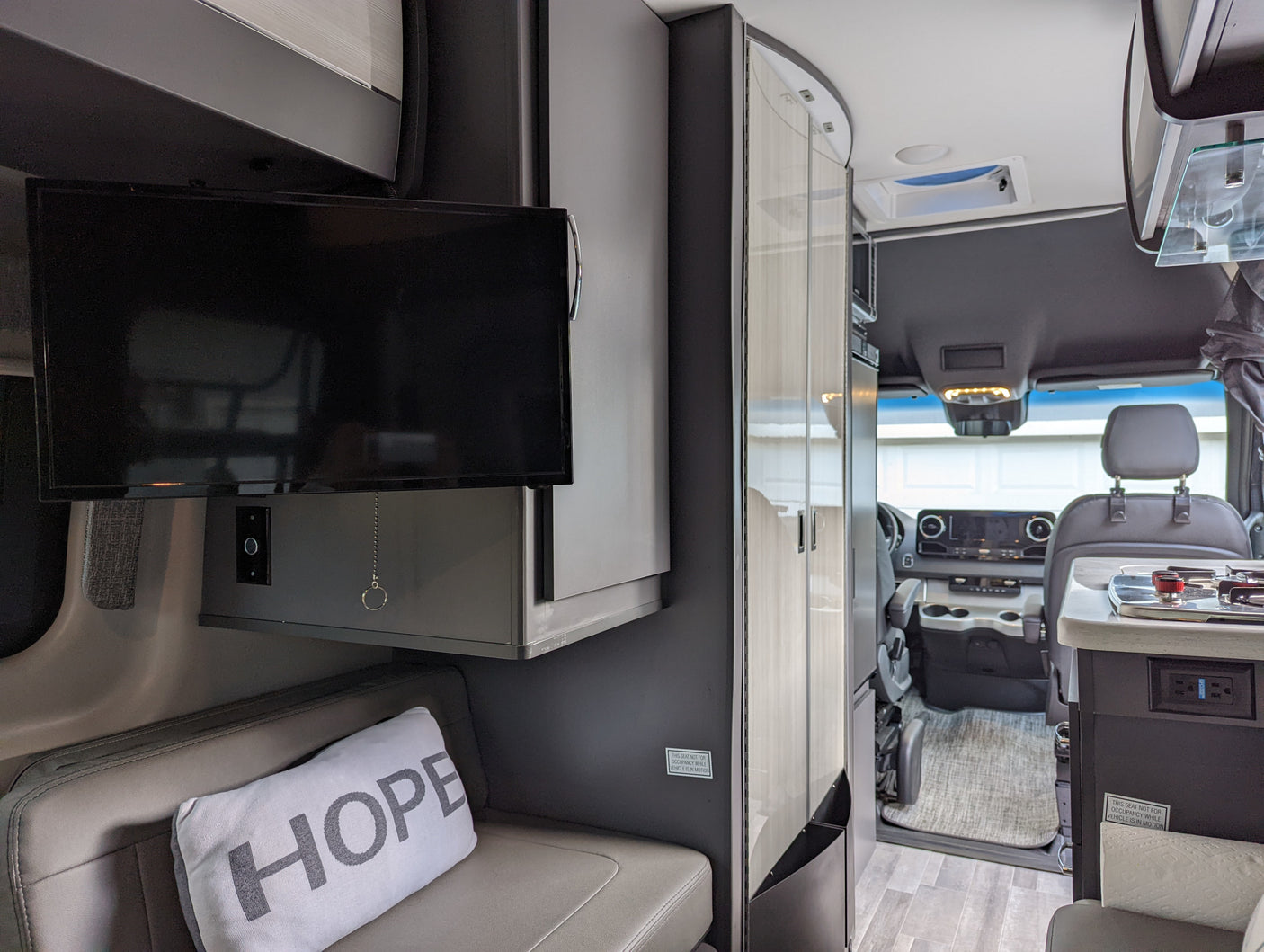 RV rental interior: A modern camper van layout featuring a TV, bench seating, and partial kitchen view leading to the cockpit.