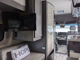 RV rental interior: A modern camper van layout featuring a TV, bench seating, and partial kitchen view leading to the cockpit.