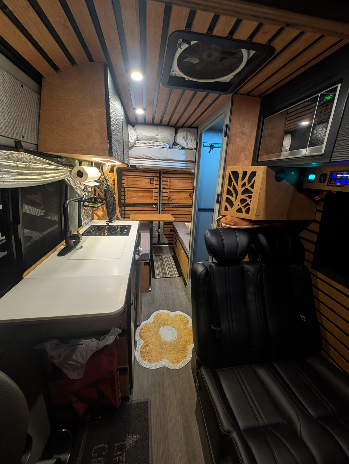 This RV rental shows a modern van interior with a kitchen, dining area, bunk bed, and comfy seating. — photo 9