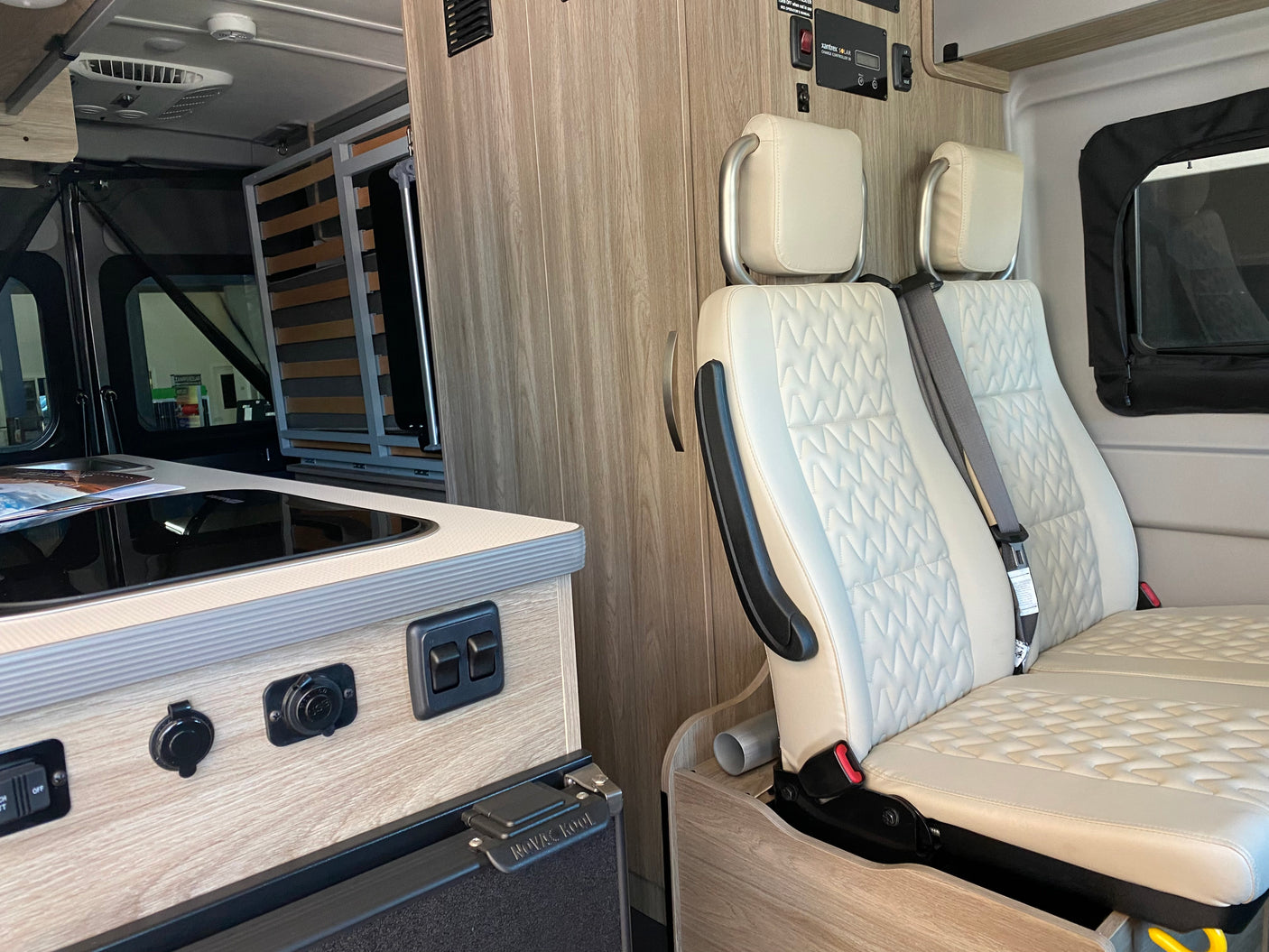 Inside a functional RV rental: discover the compact kitchen, comfortable quilted seating, and wall-mounted solar controls.