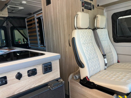 Inside a functional RV rental: discover the compact kitchen, comfortable quilted seating, and wall-mounted solar controls.