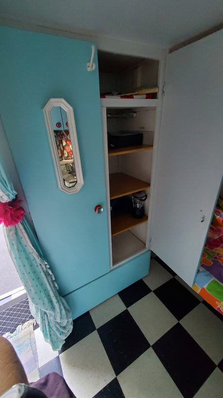 Vibrant RV rental interior: teal cabinet with mirror, organized shelves, and retro checkered flooring.