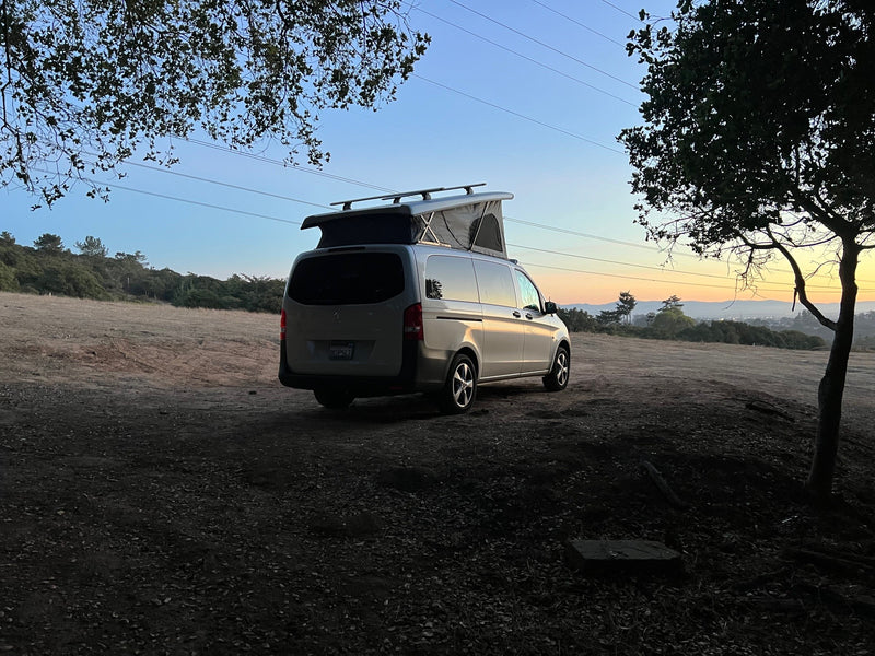 Mercedes-Benz camper van rv rental with pop-top roof open, parked at twilight with scenic hills in background. — photo 1