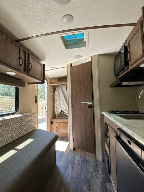Inside this RV rental: a practical kitchen with stove and sink, a cozy dinette, and wood-look flooring. Ready for travel!