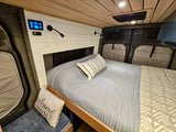 Cozy rv rental interior: comfortable bed with light blue bedding, wood ceiling, tech control panel, and adjustable reading lights.
