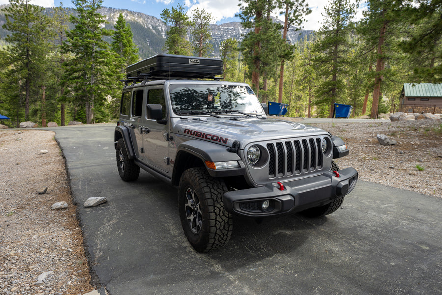 Gray Jeep Wrangler Rubicon with rooftop tent, ideal for your next RV rental adventure amidst mountains.