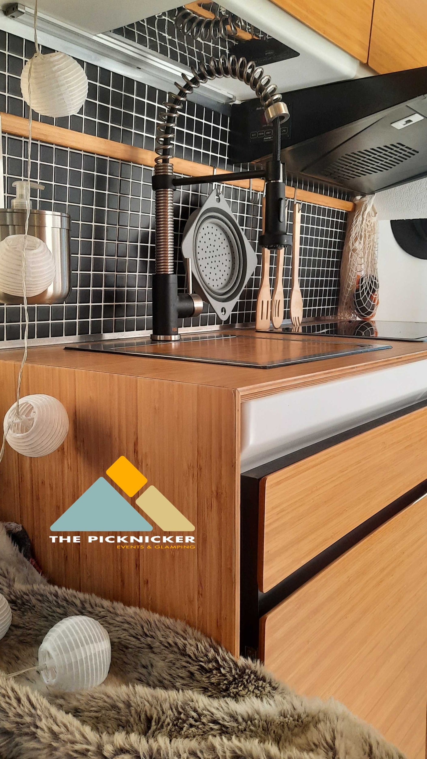Modern RV rental kitchen: sleek black tile backsplash, wooden counters, and a modern spring faucet. Cozy string lights for glamping adventures. — photo 17