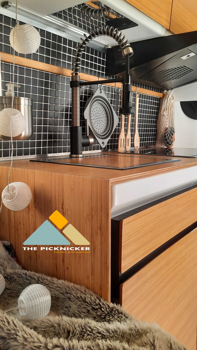 Modern RV rental kitchen: sleek black tile backsplash, wooden counters, and a modern spring faucet. Cozy string lights for glamping adventures. — photo 17