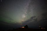 Milky Way and green airglow illuminate an RV rental, car, and tree on a hill, creating a stunning starry night camp scene.