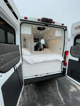 Modern RV rental interior with a cozy white bed, wood paneling, and ample storage for comfortable travel.