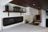A spacious & modern RV rental interior with a light gray bed, kitchen area with white subway tiles, & wood ceiling.