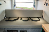 RV rental interior: A cozy bench seat with seatbelts, offering a scenic view out the back doors to water.