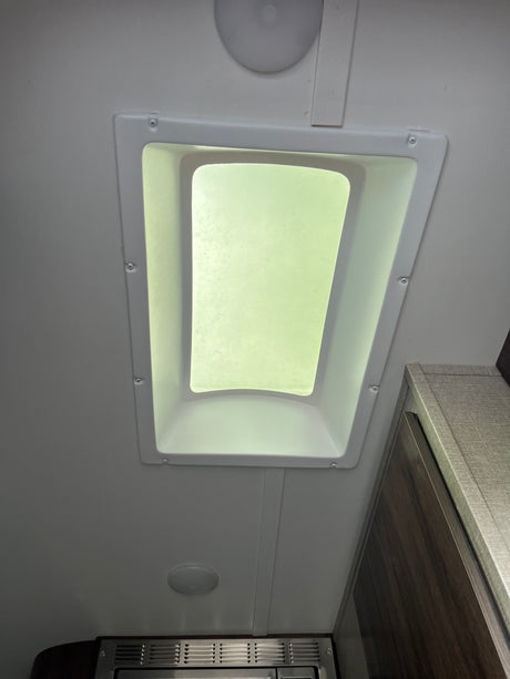Bright RV rental interior showcasing a ceiling skylight, lighting, and upper cabinetry, offering natural illumination.