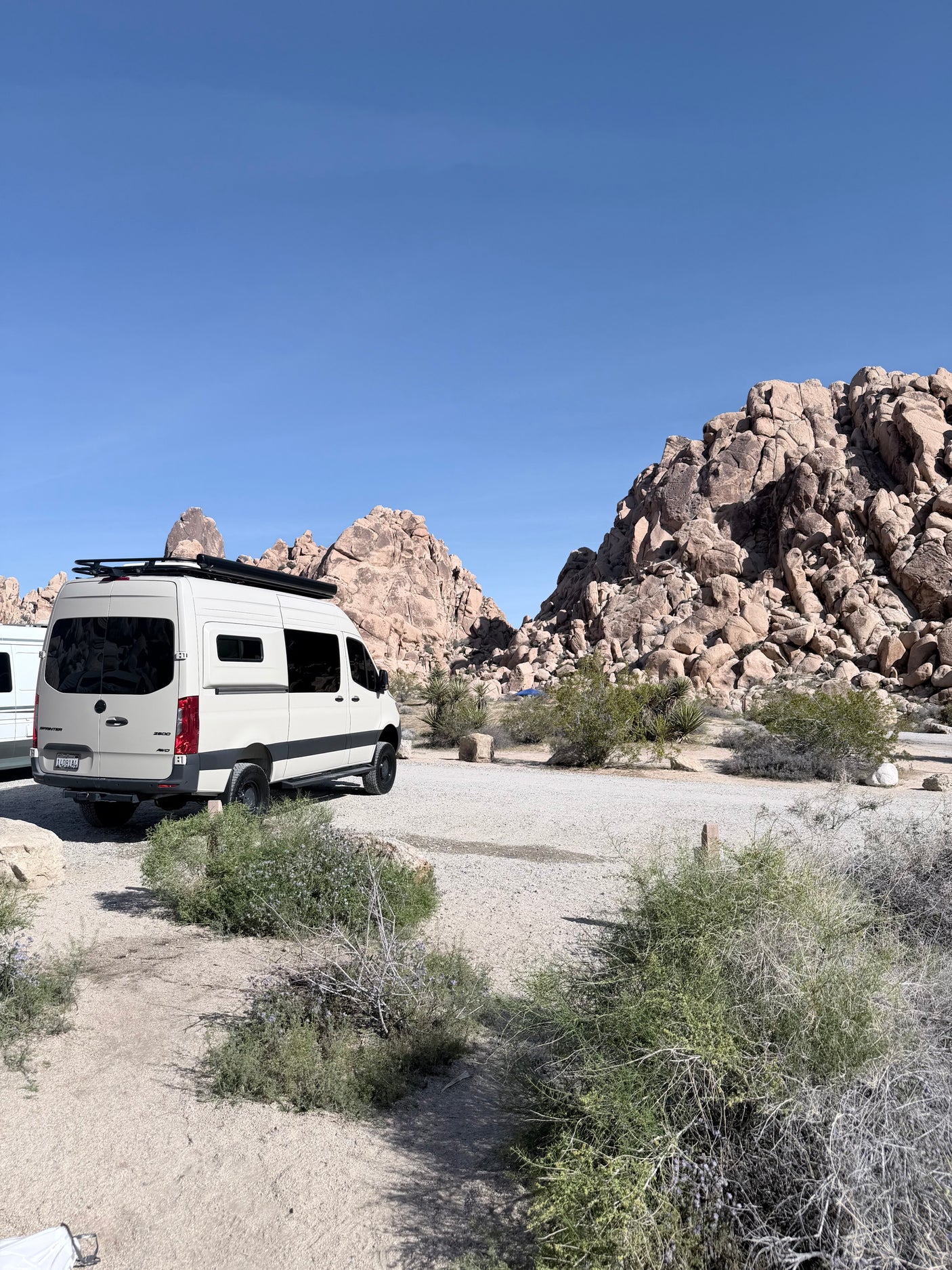 White rv rental camper van in a scenic desert landscape with large rock formations under a clear sky.