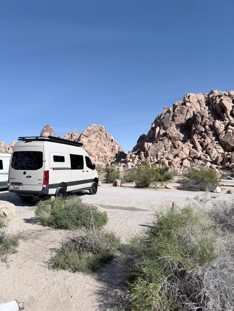 White rv rental camper van in a scenic desert landscape with large rock formations under a clear sky.