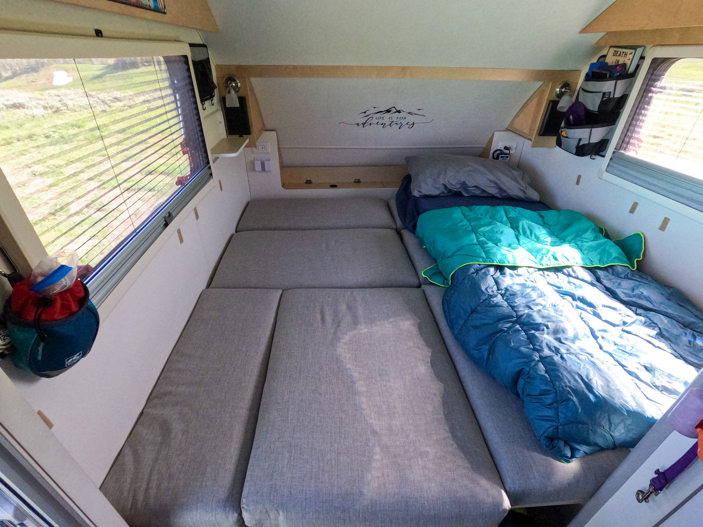 Inside an RV rental: a comfortable bed with sleeping bags, window view, and storage for your next adventure.