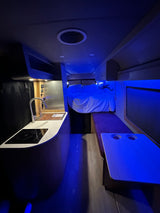 RV rental interior: A modern camper van setup with a functional kitchen, elevated bed, and striking blue ambient lighting.