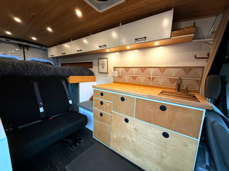 Cozy rv rental interior featuring a wood ceiling, kitchenette, bed, and seating with a custom patterned backsplash.