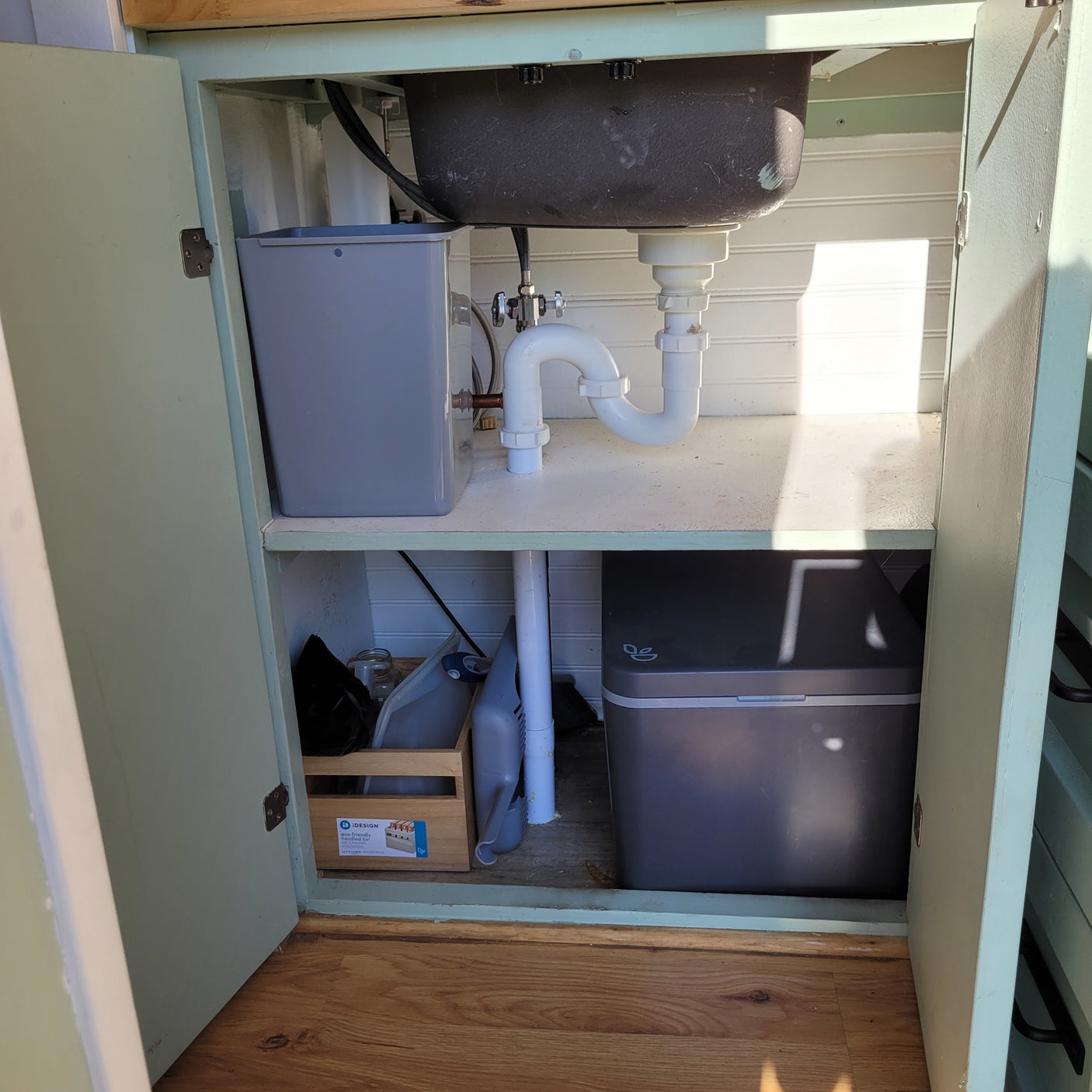RV rental under-sink cabinet: Dark sink basin, white P-trap plumbing, and compact water and storage solutions.