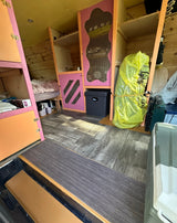 Custom built RV rental interior with pink and orange accents, bed, and storage. Ideal for travel.