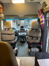RV rental interior view: the front cabin features tan swivel seats, a dashboard with controls, and travel essentials.