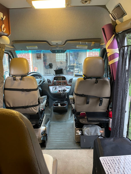 RV rental interior view: the front cabin features tan swivel seats, a dashboard with controls, and travel essentials.