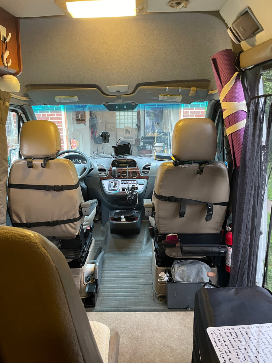 RV rental interior view: the front cabin features tan swivel seats, a dashboard with controls, and travel essentials.