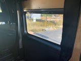 Interior view of an rv rental showing a black seat, window with a "NO PARKING" sign outside, and wood paneling.
