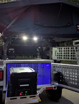 Off-road camper/rv rental setup: rooftop tent, bright lights, portable fridge, and illuminated gear storage.