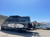 Custom RV rental van with surfboards and bikes by the scenic ocean and mountains. Ideal for adventure travel.