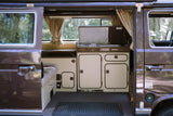Interior view of a Westfalia RV rental, showing its practical kitchenette with stove, sink, cabinets, and a cozy bench area.