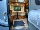 Inside a modern rv rental: a well-lit dinette with U-shaped seating, wood flooring, and a view to nature from the window.