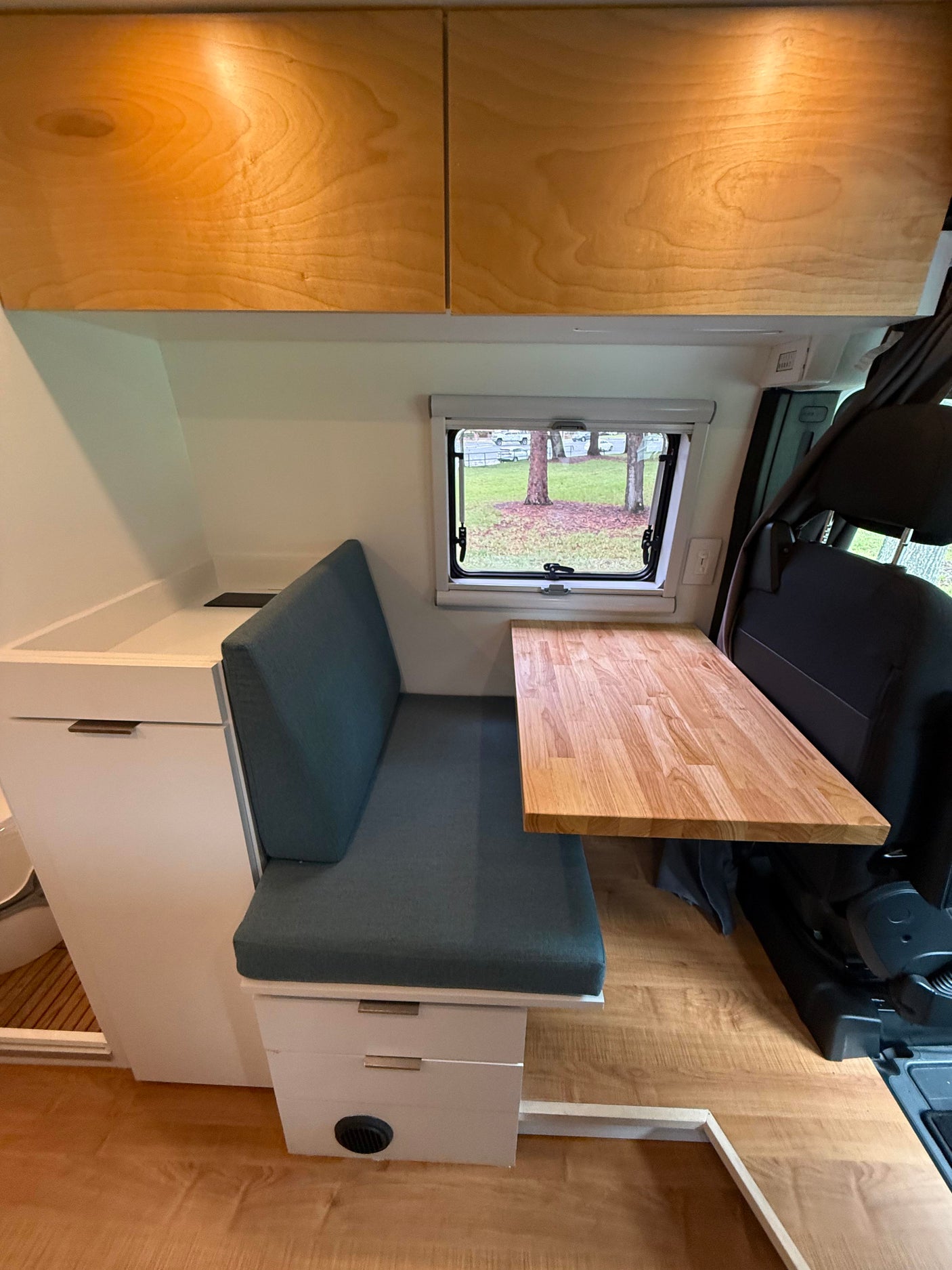 Inside this cozy RV rental, a dinette boasts a comfy bench, wood table, and ample overhead storage cabinets.