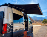 Storyteller Overland Beast RV rental camper van with open door and extended awning, parked in a scenic mountain setting.