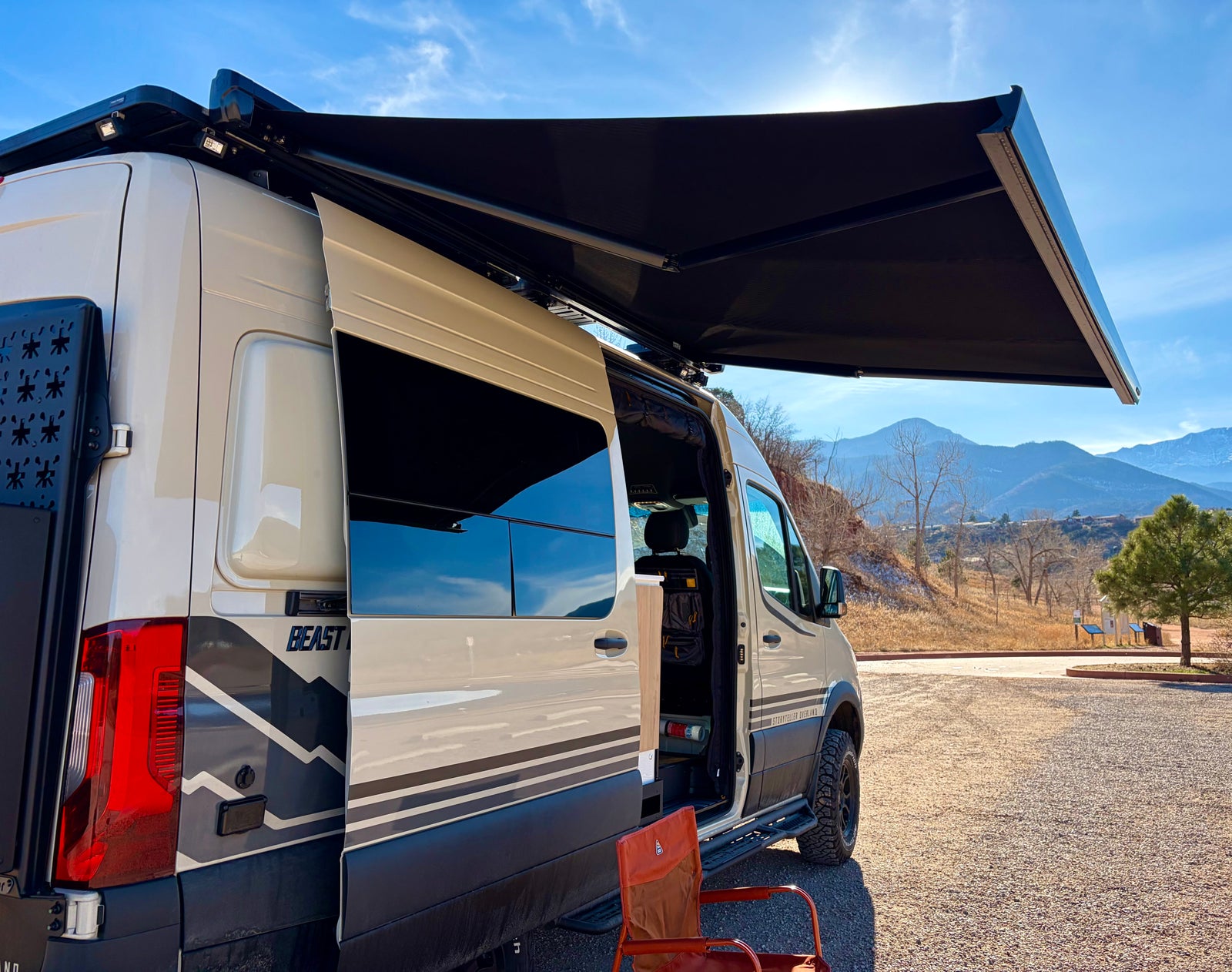 Storyteller Overland Beast RV rental camper van with open door and extended awning, parked in a scenic mountain setting.
