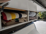RV rental overhead storage: White cabinets open to reveal colorful striped blankets and soft pillows, ready for adventures.