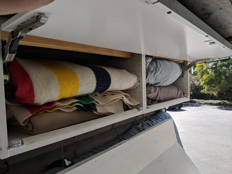 RV rental overhead storage: White cabinets open to reveal colorful striped blankets and soft pillows, ready for adventures.