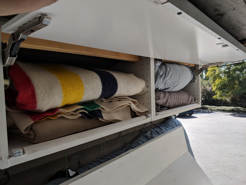RV rental overhead storage: White cabinets open to reveal colorful striped blankets and soft pillows, ready for adventures. — photo 15