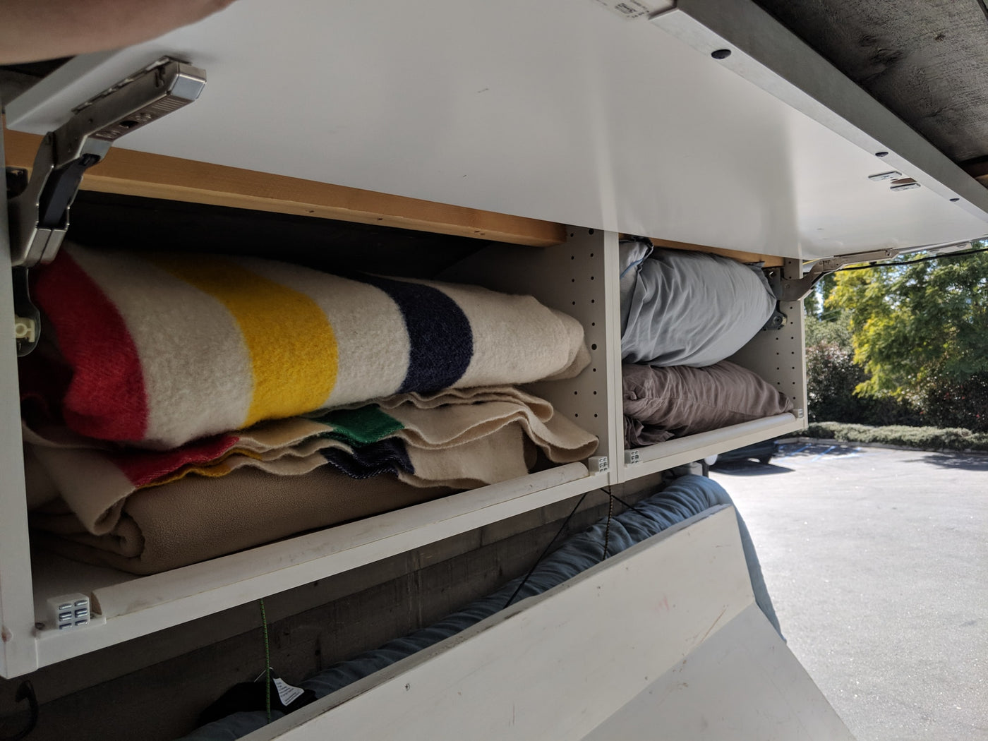 RV rental overhead storage: White cabinets open to reveal colorful striped blankets and soft pillows, ready for adventures. — photo 35