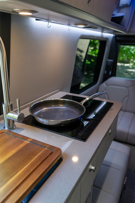 Modern RV rental kitchen with cooktop, pan, faucet, and cutting board for on-the-go cooking.