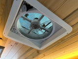 Looking up at a MaxxAir fan installed in the wood-paneled ceiling of an rv rental, showing the sky through the screen.