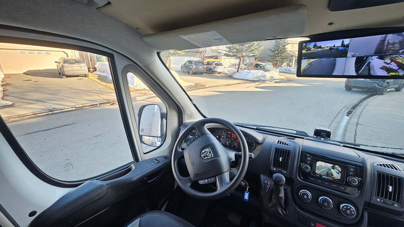 Inside an rv rental Ram ProMaster van, the driver's view includes dash, steering, and a multi-camera display of the street.
