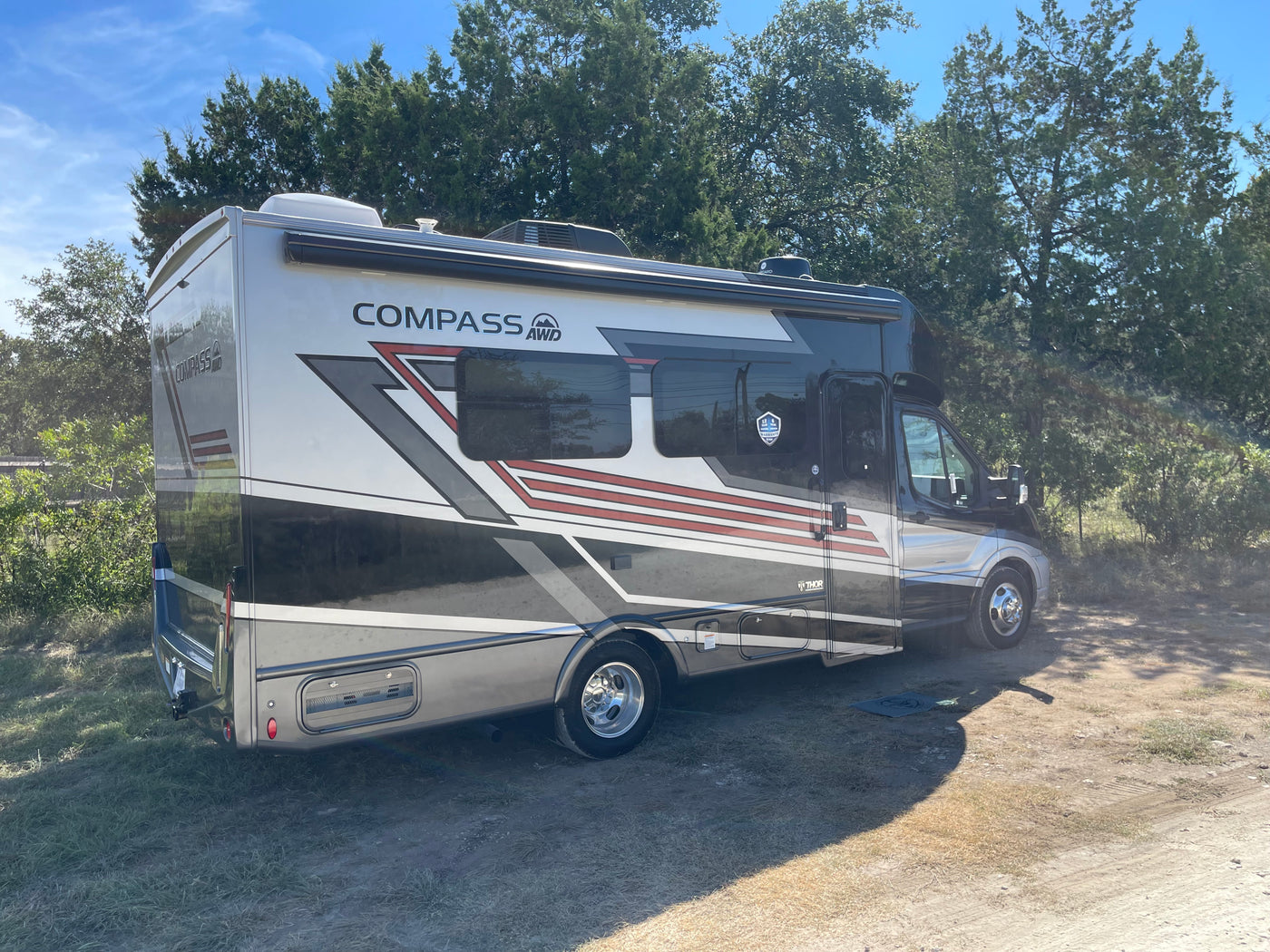 Modern Thor Compass AWD RV rental, silver and black with accent stripes, parked on a dirt lot under blue sky. — photo 4