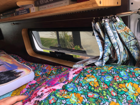 Relaxing RV rental interior: colorful quilted bed, window, and books on a shelf for cozy travels.