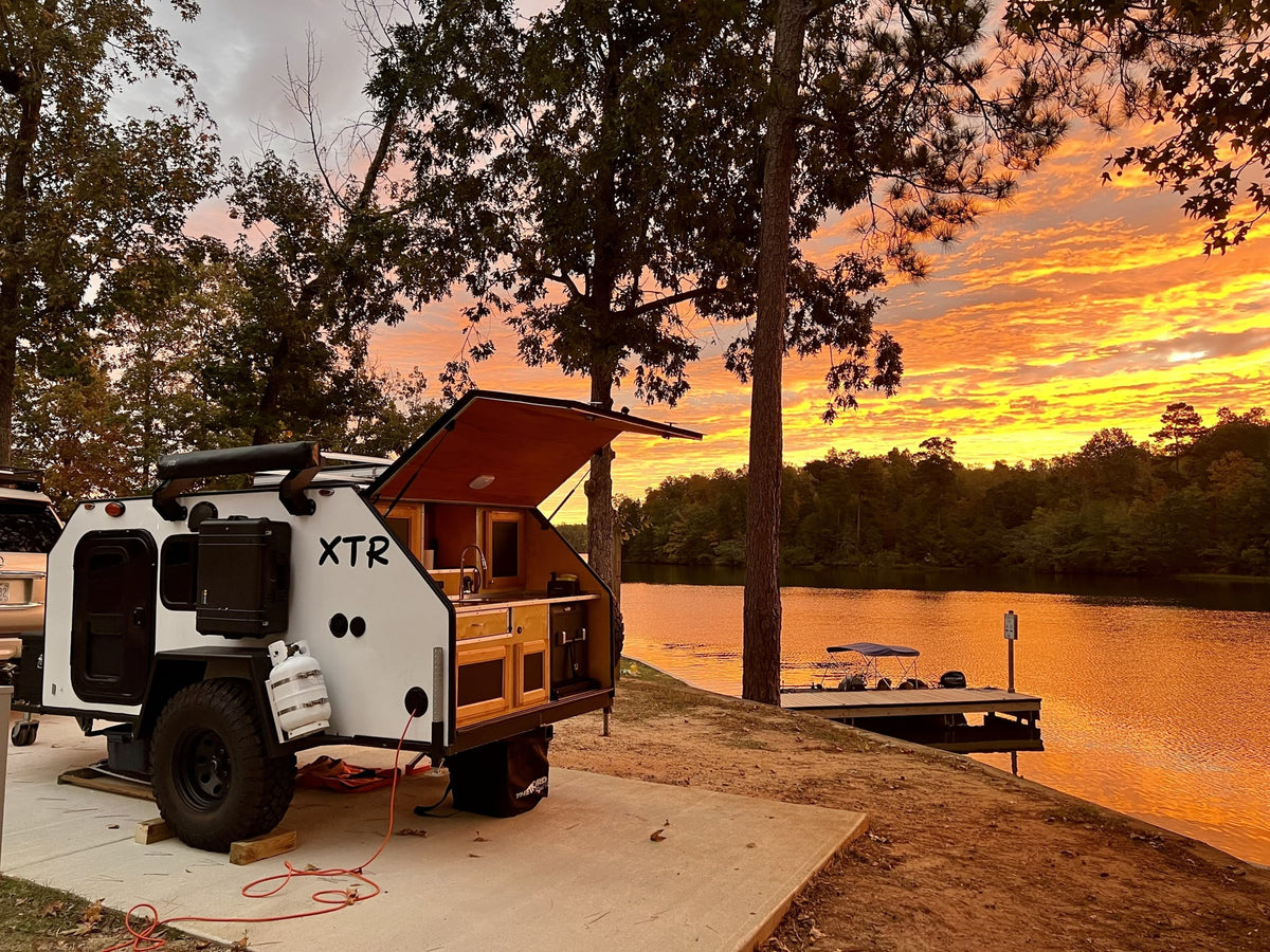 Enjoy breathtaking sunsets from this XTR teardrop camper by the lake. Perfect for an unforgettable rv rental camping trip!|A rugged white XTR off-road teardrop camper with large tires